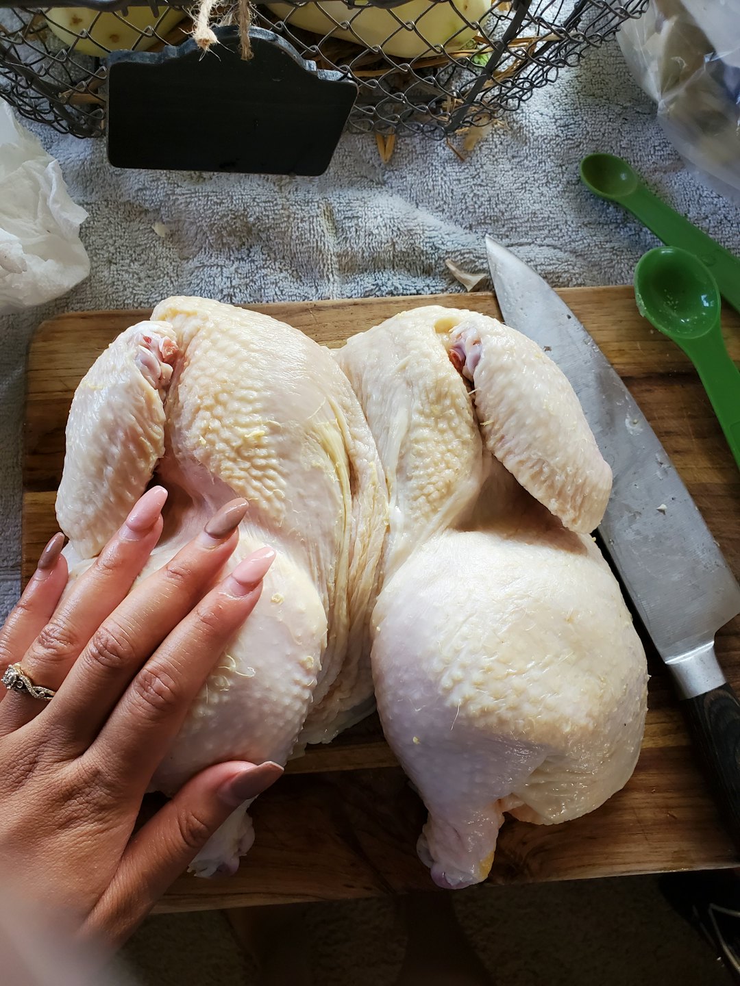 A hand prepares raw chicken on a wooden cutting board.