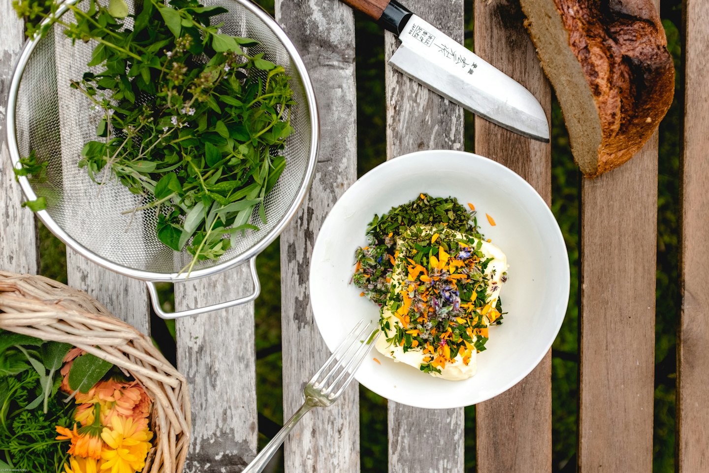 Fresh herbs, butter, bread, and flowers on a wooden table.